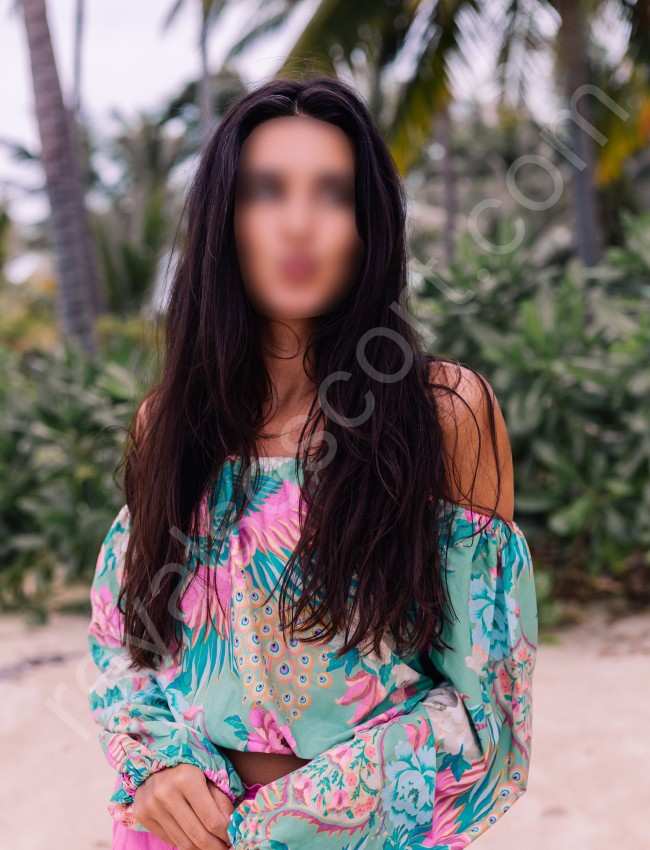 Independent Escort & Call Girl Aarvika stating front of plant wearing colourful top and smiling