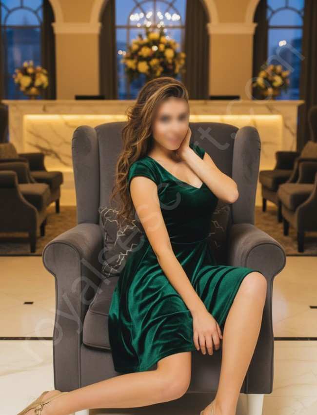 High Profile call girl Escort Avenira sitthing on sofa wearing green gown 