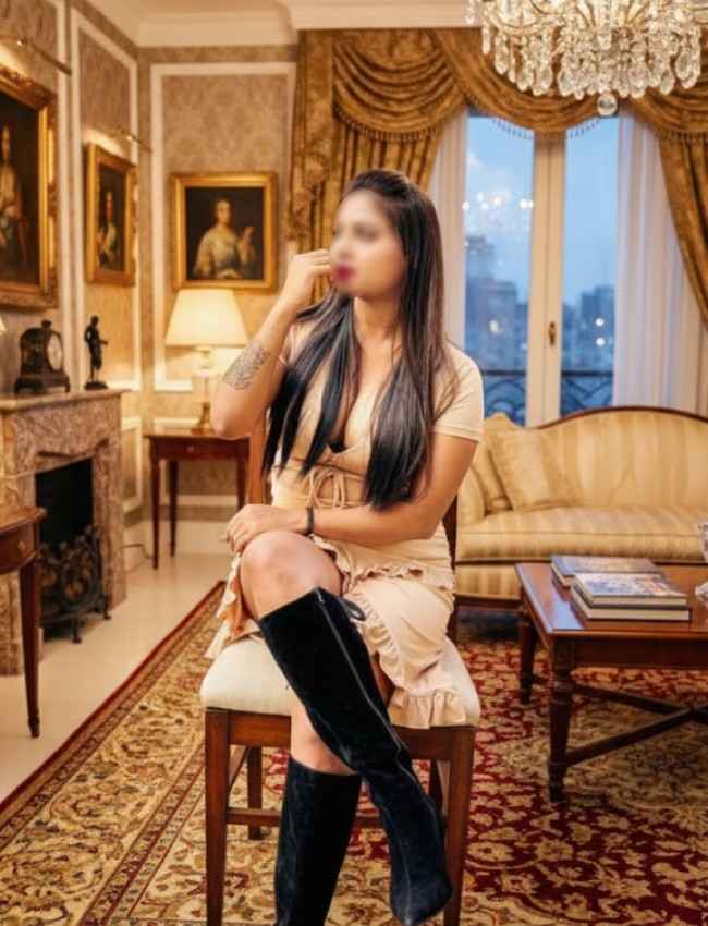 VIP Escort Drishti in a luxury room sitting on chair wearing boots 